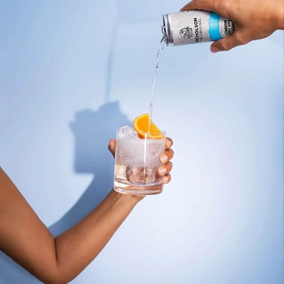 A hand pouring a drink into a glass in a blue campaign image