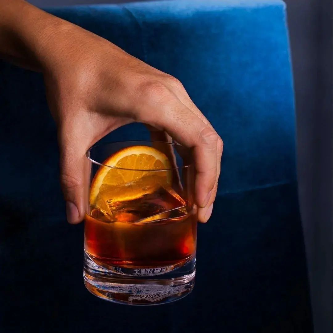A hand holding a whiskey glass in a warm campaign photograph